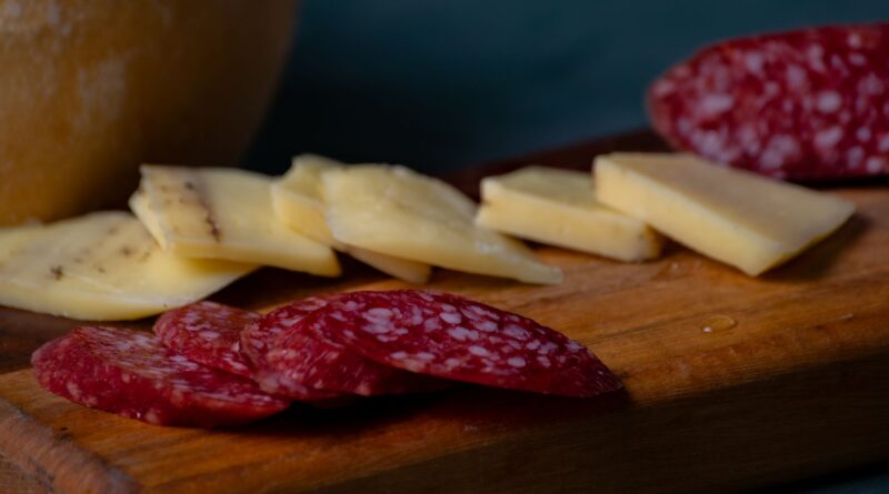 Close-up of sliced cheese and salami on a wooden platter, perfect for appetizers.