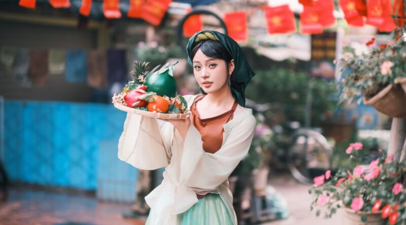 A woman in traditional dress holds a colorful food platter during festive celebrations outdoors.