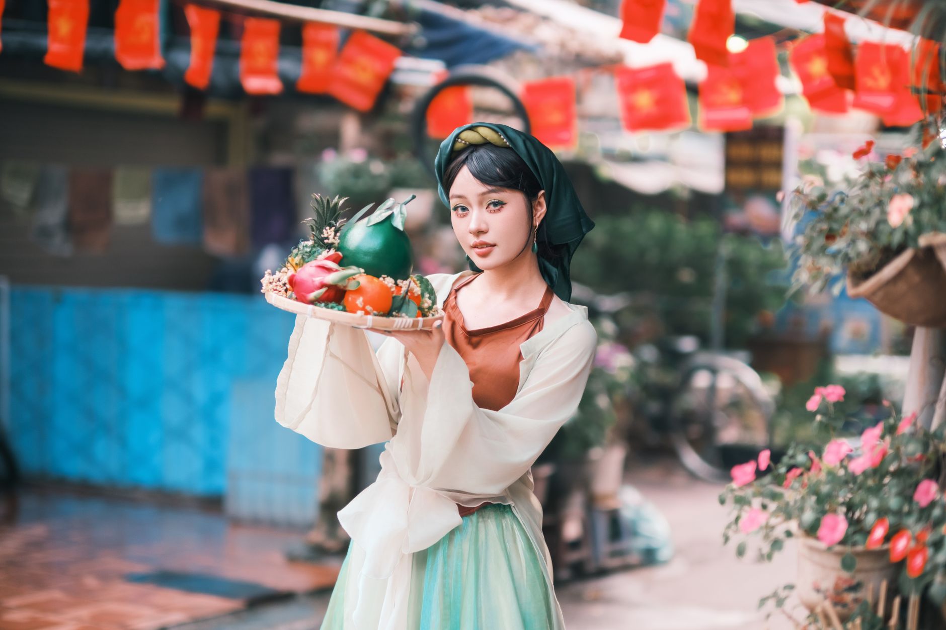 A woman in traditional dress holds a colorful food platter during festive celebrations outdoors.