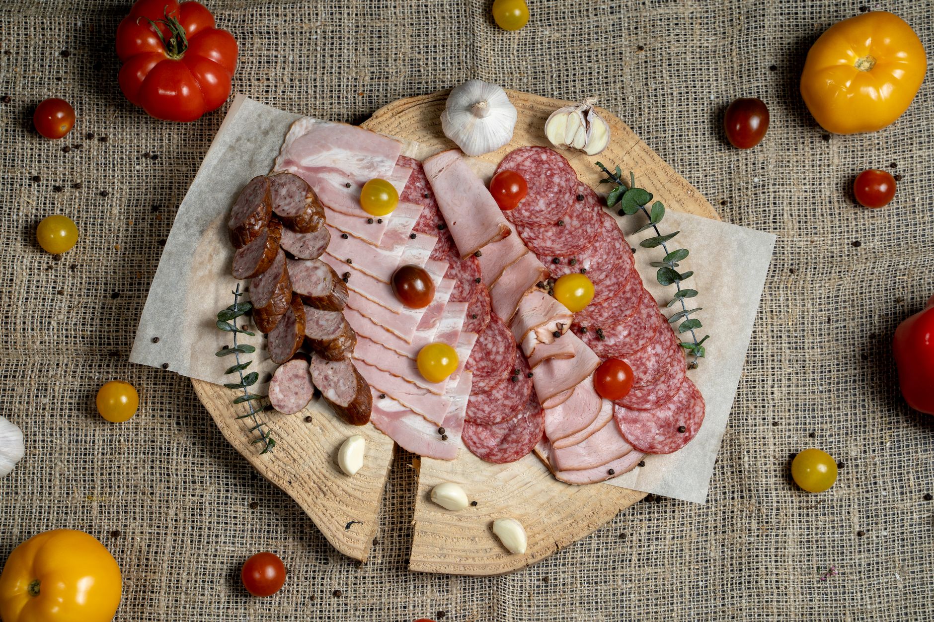 A high-angle view of assorted cured meats and fresh tomatoes on a rustic wooden board.