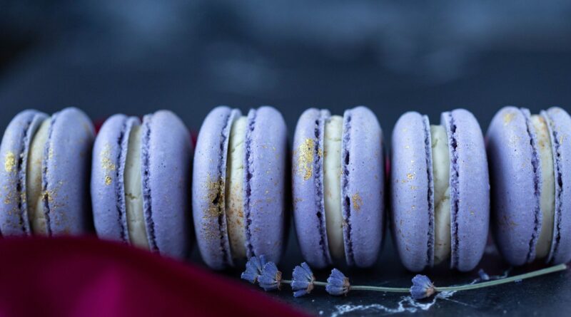 Set of delicious sweet macaroons in violet color with white cream served on table in bakery with flower