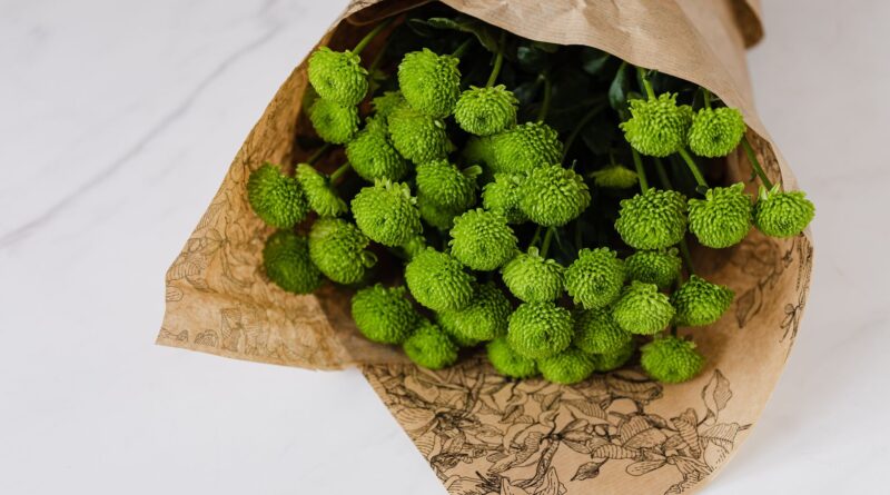 Bunch of craspedia wrapped in paper flower packaging placed on white marble table