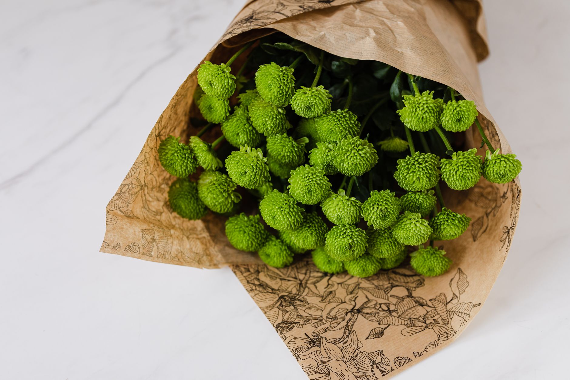 Bunch of craspedia wrapped in paper flower packaging placed on white marble table